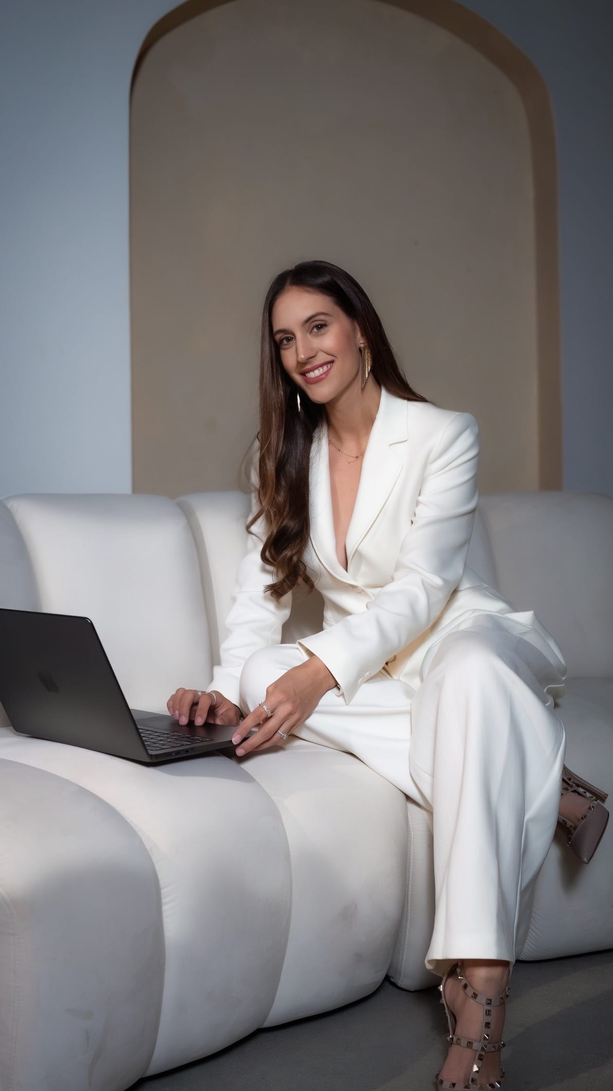 Veronica Lopez-Calleja, Esq., CEO & Founding Attorney, smiling at her laptop in a white suit